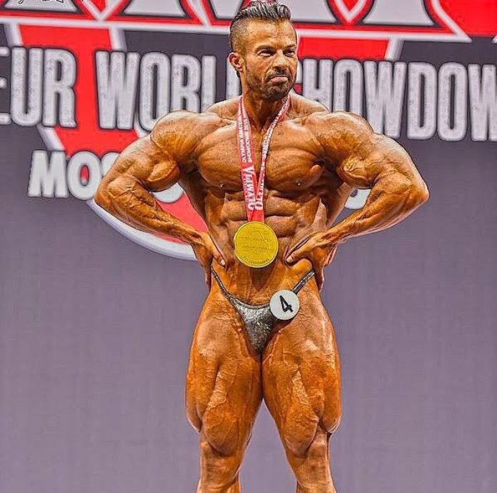 Babak Akbarniya wearing a golden medal around his neck, doing lat spread pose