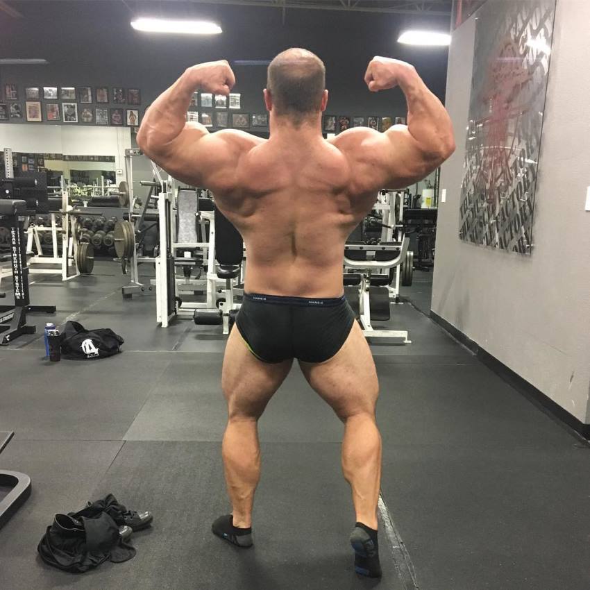 John Jewett in a shirtless back double biceps pose in the gym, looking massive