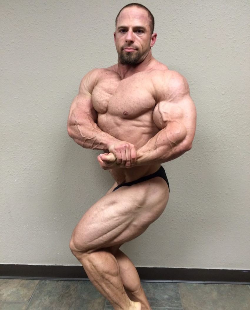 John Jewett in a side chest pose, flexing his big and aesthetic arms, legs, and chest