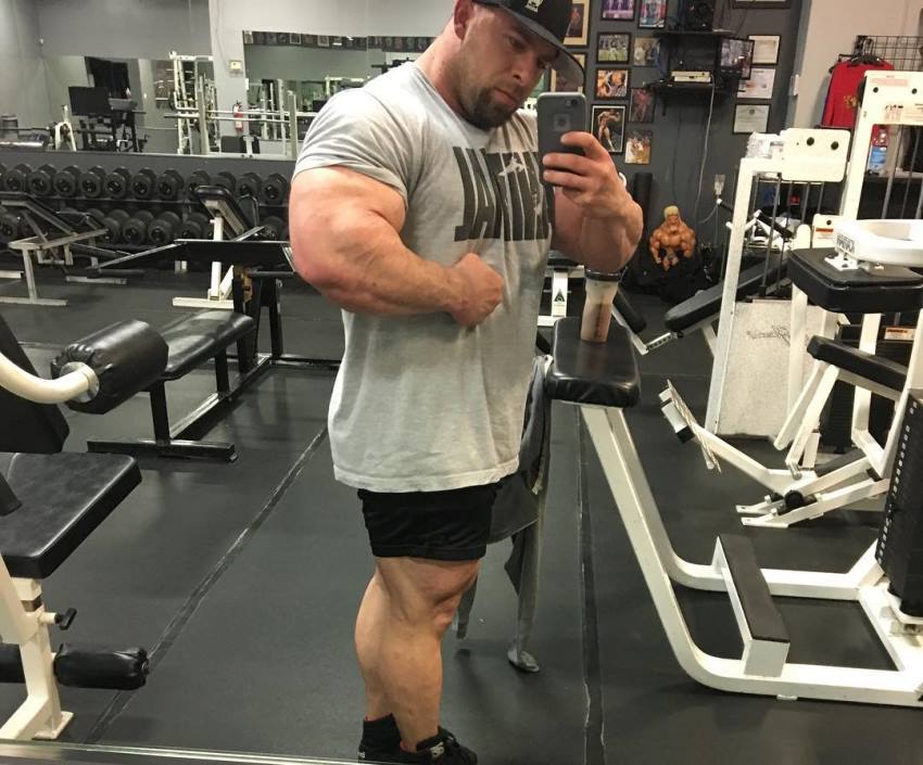 John Jewett flexing his arms while taking a selfie in the gym mirror