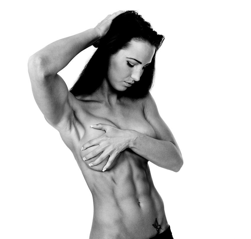 Karen Lind Thompson posing naked, covering her breasts with one of her hands, while the other one is in her hair, showing her ripped abs and obliques