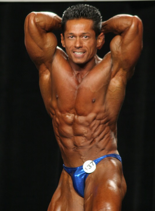 Leonardo Pacheco during his younger days in bodybuilding, flexing his abs on the stage