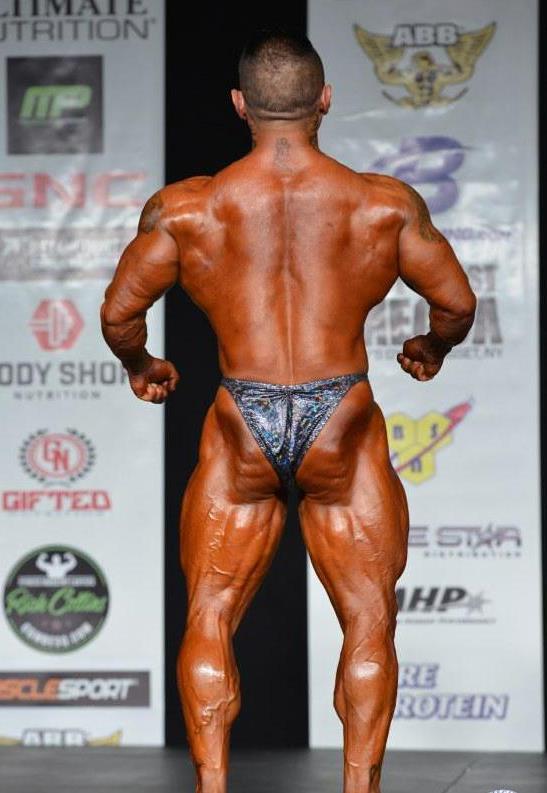Leonardo Pacheco spreading his lats and arms on the bodybuilding stage, looking muscular