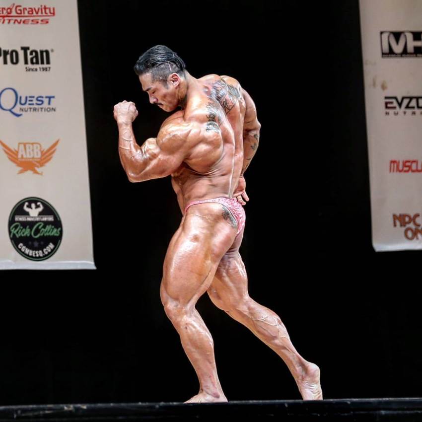 Nam Eun Cho posing on the bodybuilding stage, his back and legs looking massive