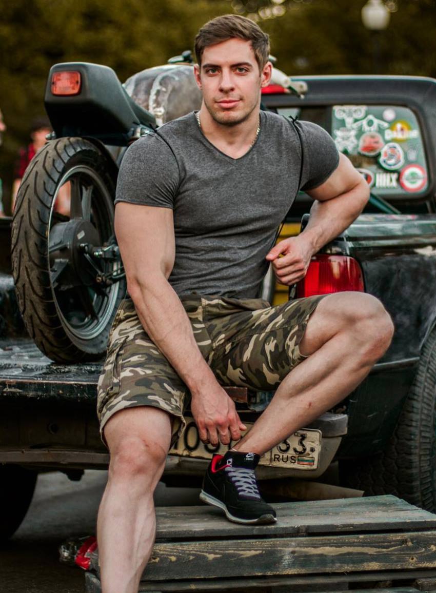 Nikolay Kuleshov sitting on the rear end of a truck, his muscles showing off through clothes
