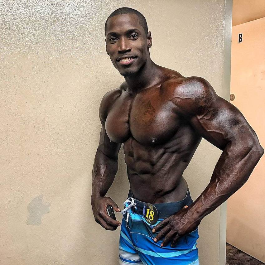 Otto Montgomery posing for the camera in sea blue trunks, tanned up, looking extremely ripped and big