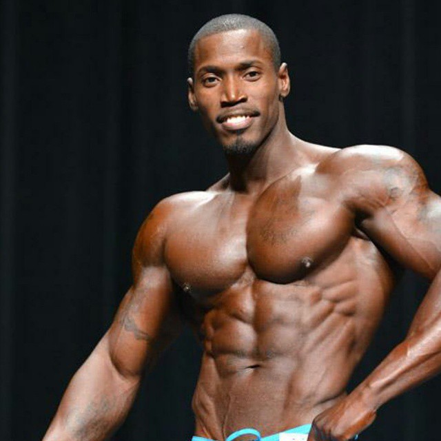 Otto Montgomery flexing his abs, arms, and pecs on the stage, smiling at the audience