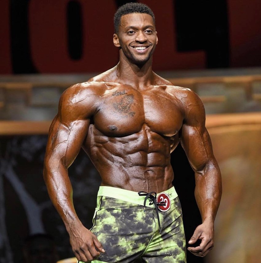 Raymont Edmonds smiling at the audience, as he shows his oiled up, tanned up, and ripped physique