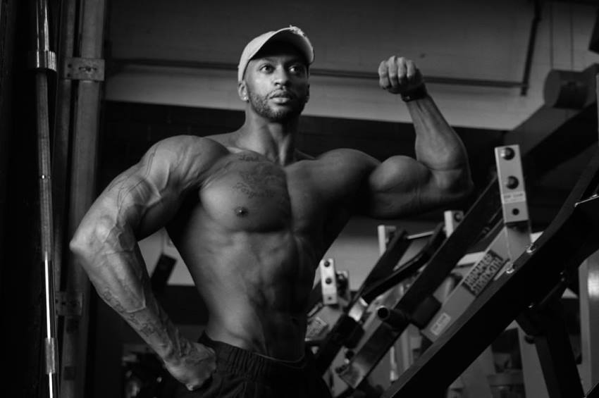 Black and white picture of Raymont Edmonds flexing his biceps in a gym, looking at the distance