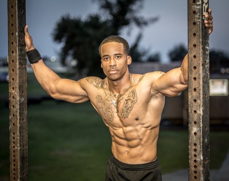 Andre Smith holding onto two iron bars, being shirtless, looking at the camera