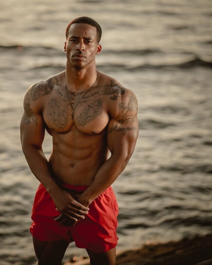 Andre Smith standing by the beach in red shorts, looking fit and ripped