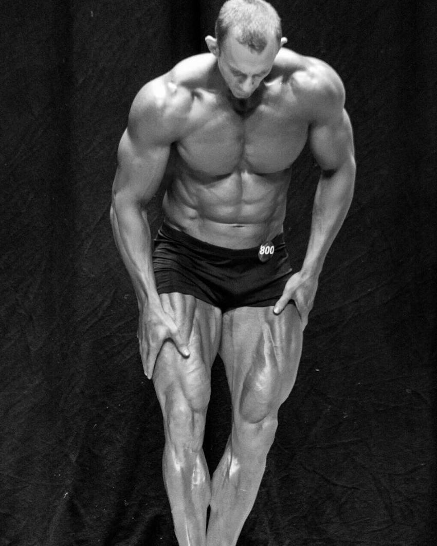 Brandon Gerdes flexing his legs and abs on the stage, looking down