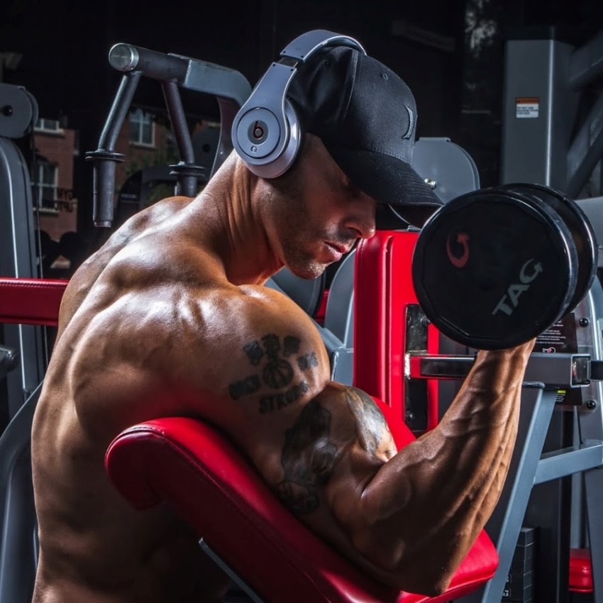 Brian Barthule doing seated dumbbell biceps curls, looking lean and muscular