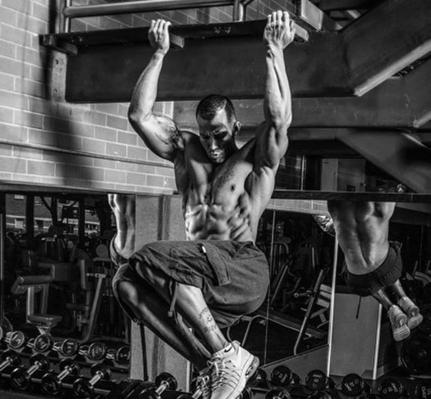 Brian Barthule performing hanging leg raises in the gym while displaying his awesome abs