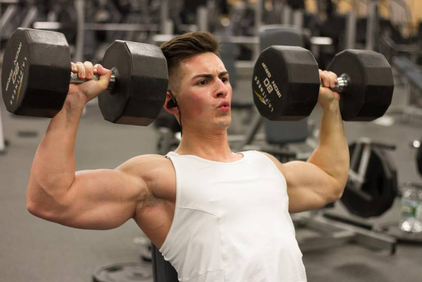 FaZe Censor doing a shoulder press exercise in the gym, wearing a sleeveless white shirt