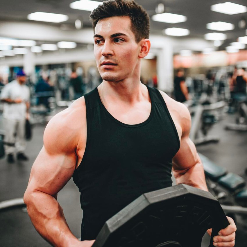 FaZe Censor holding a weight plate in the gym, wearing a black tank top, looking muscular and ripped