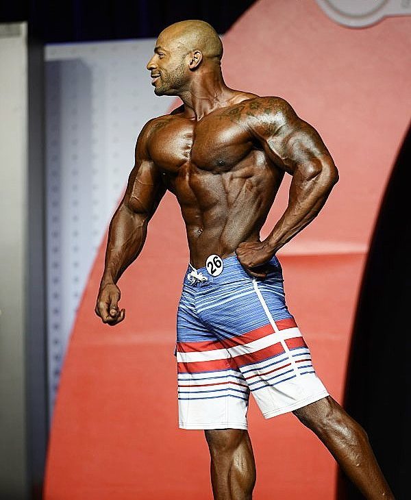 Jacques Lewis doing a side pose on the Olympia stage, looking ripped and muscular