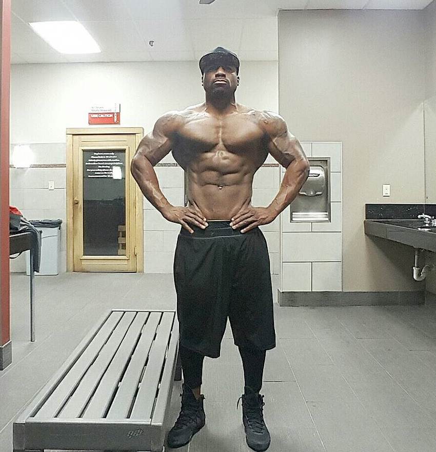 Jacques Lewis posing in the gym locker room, spreading his aesthetic lats and arms