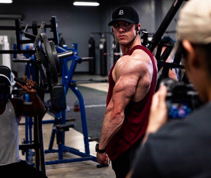 Jonny Bernstein wearing a red tank top, flexing his triceps and shoulders