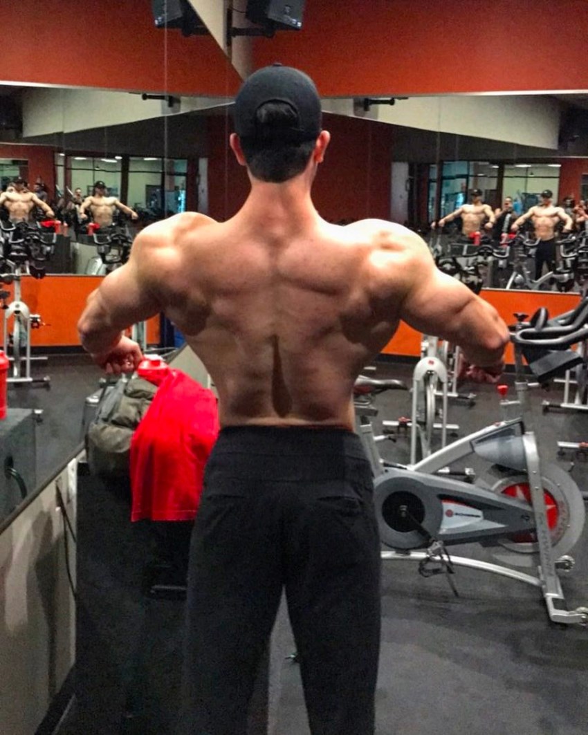 Shirtless Jonny Bernstein spreading his lats in the gym, showcasting his ripped back