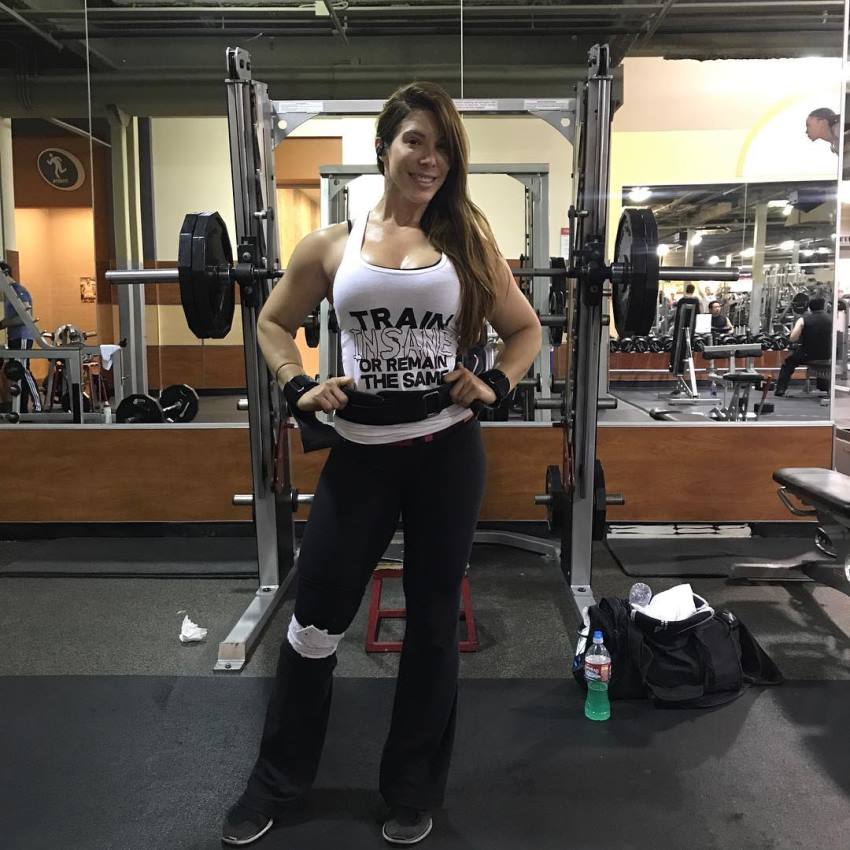 Juliana Barreto smiling at the camera, standing in front of a squat rack in the gym