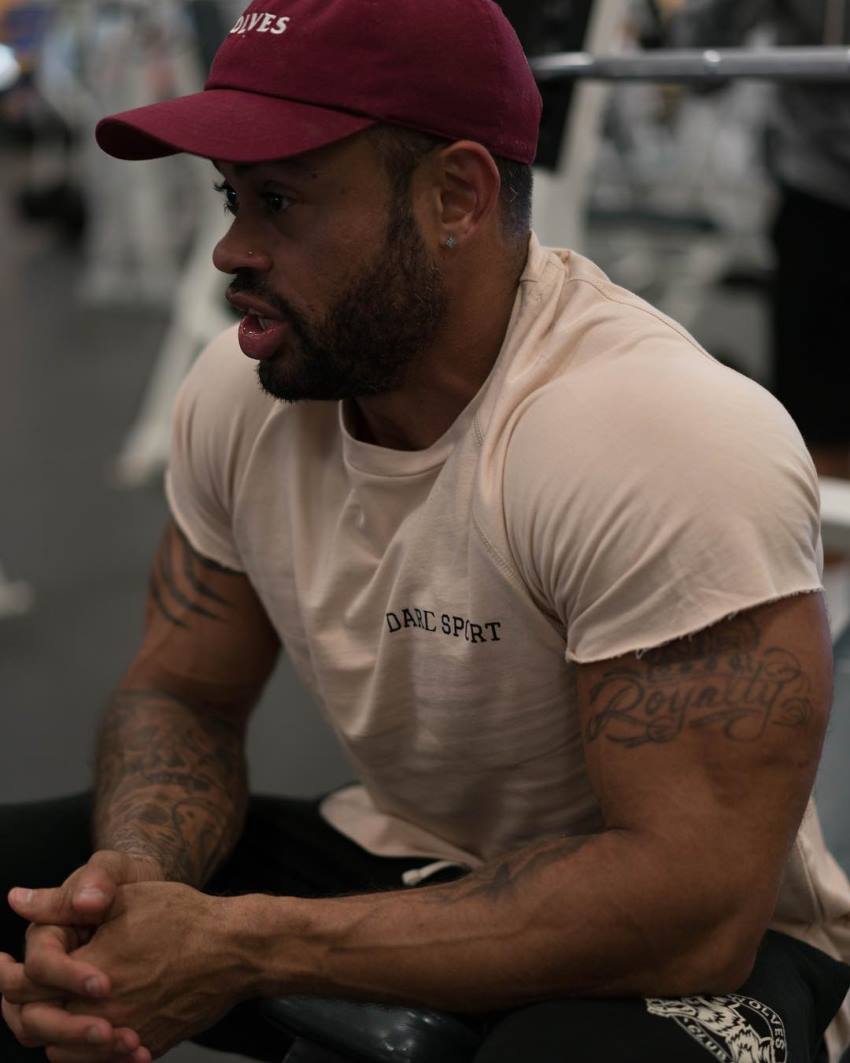 Kai Spencer sitting in the gym, his arms looking big and muscular in a white t-shirt