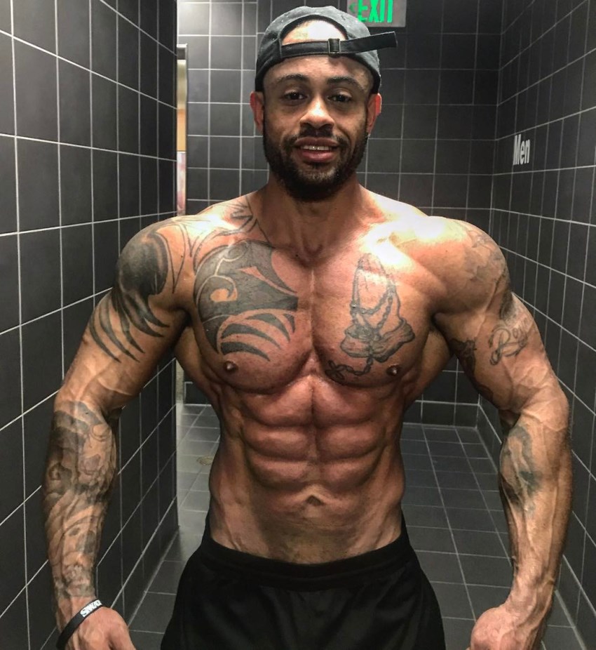 Kai Spencer spreading his arms and lats wide from the front, looking lean, ripped, and muscular