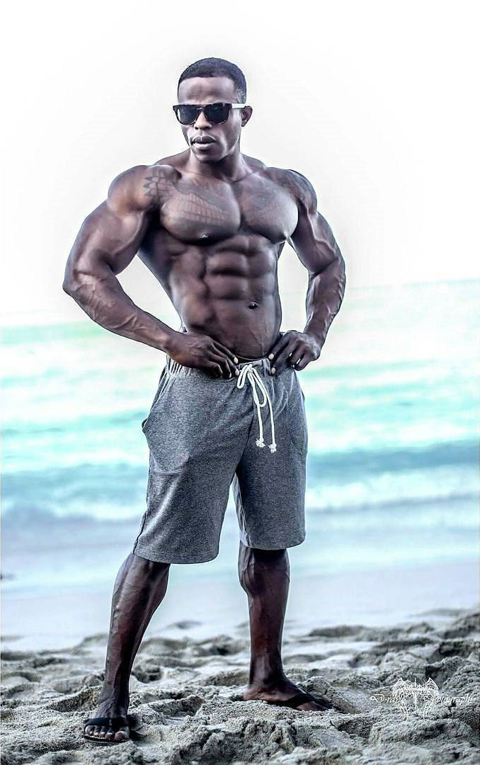 Andre Ferguson posing next to a beach with his short off looking ripped and muscular