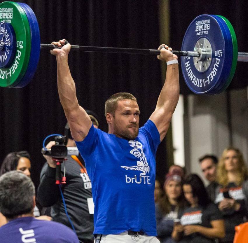 Chris Powell doing an overhead barbell press in a CrossFit competition