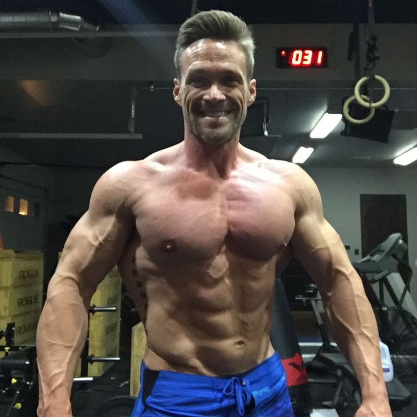 Chris Powell posing shirtless in the gym, looking muscular and ripped