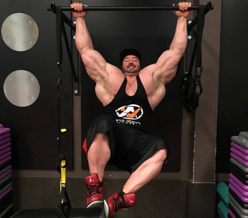 Craig Golias ganging on a bar in black tank top, his lats and arms looking enormous