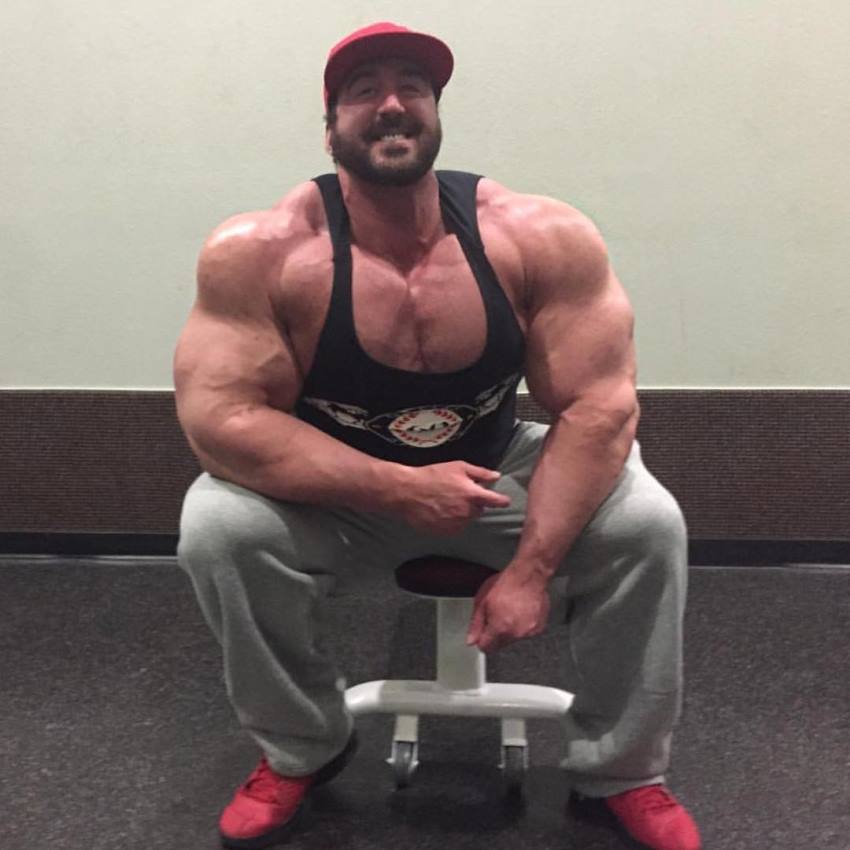 Craig Golias sitting on a bench posing for the camera and flexing his big arms