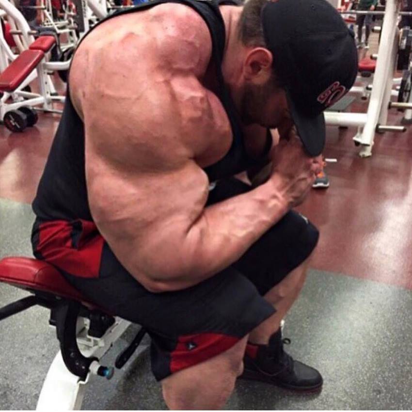 Craing Golias sitting on a bench in the gym, his arms and shoulder looking massive