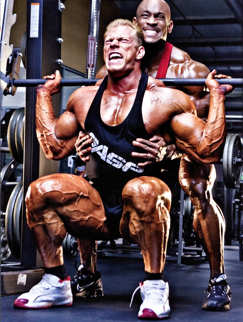 Dennis Wolf doing squats with a pained expression on his face, and a spotter behind him