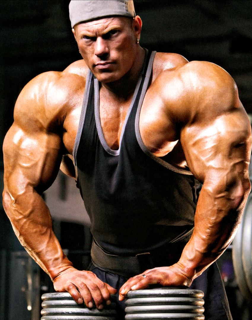 Dennis Wolf posing for a photo, leaning against dumbbells, looking massive and aesthetic