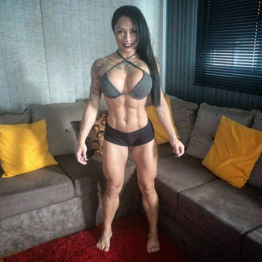 Elah Bittencourt standing in the room showing her flexed abs and legs