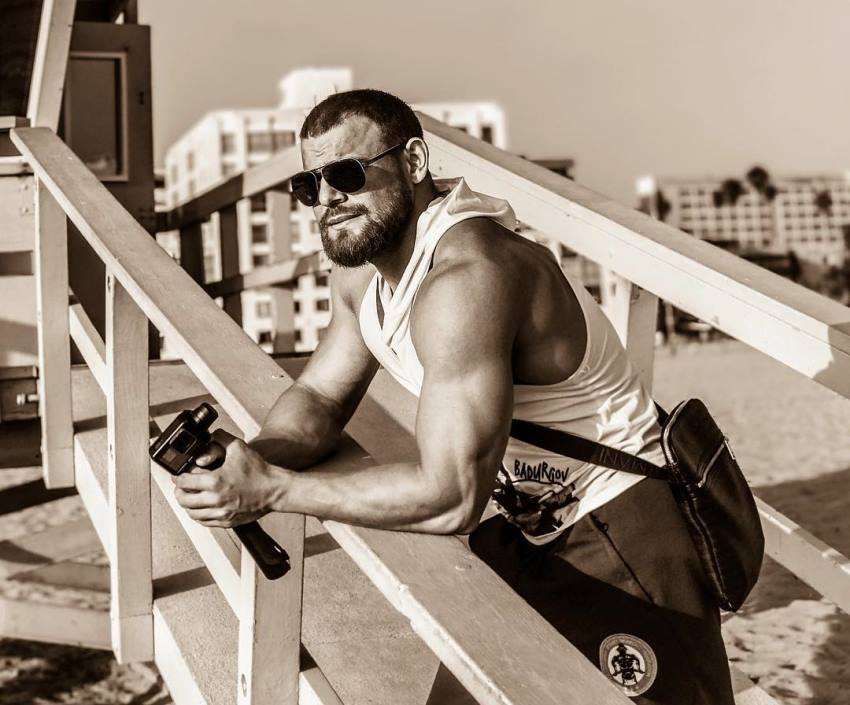 Islam Badurgov leaning against a fence on the beach, looking at the distance