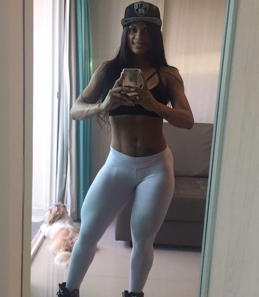 Jeniffer Alves taking a selfie of her flexed abs and legs in white leggings