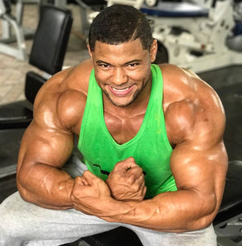 Robert Galva sitting on a bench in the gym, flexing his muscular arms