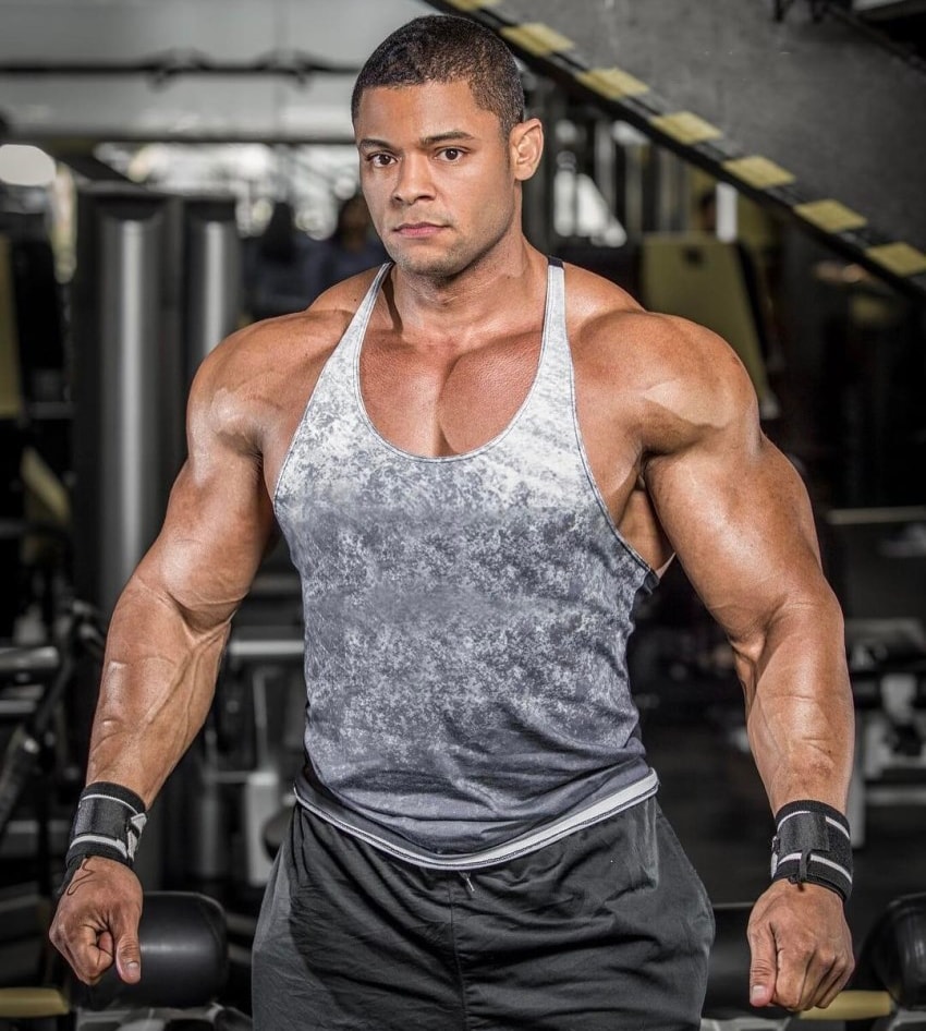 Robert Galva standing in the gym in a grey tank top, looking muscular and ripped