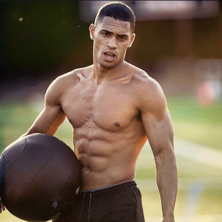 Ryan Tremaine Klarenbach holding a black medicine ball with one of his hands, looking ripped and aesthetic