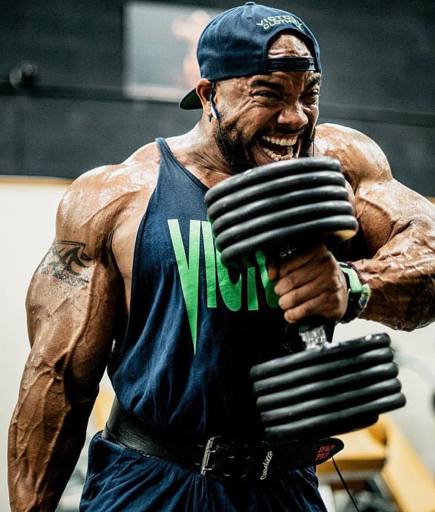 Sergio Oliva Jr doing hammer curls with a pained grimace