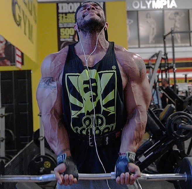 Sergio Oliva Jr doing barbell biceps curls with a pained expression on his face