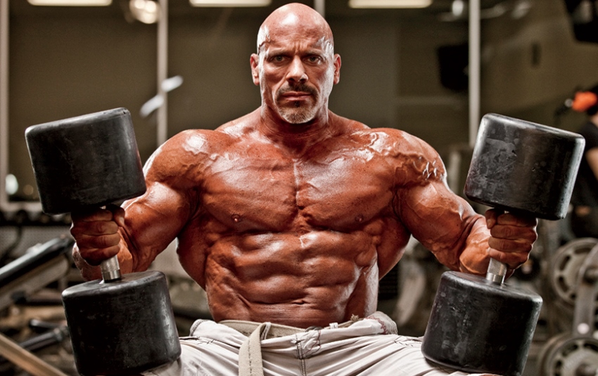 Stan Efferding shirtless preparing to lift two heavy dumbbels in the gym