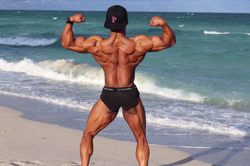 Ahmad DeGuzman doing a back double biceps flex on the beach