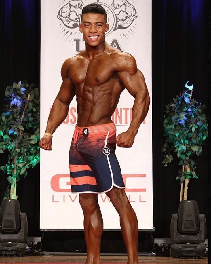 Ahmad DeGuzman on the Men's Physique stage smiling at the audience