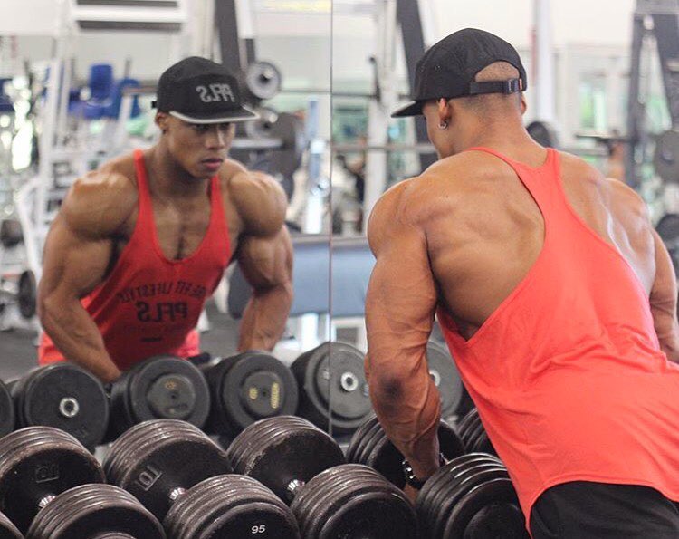 Ahmad DeGuzman looking at himself in the mirror while holding dumbbells