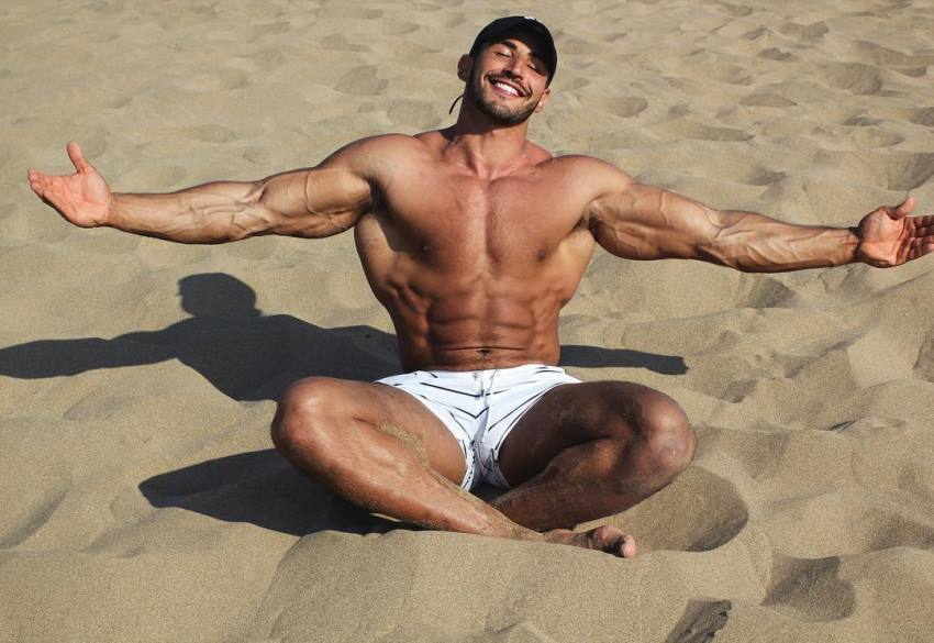 Amin Elkach sitting shirtless on the sand and soaking up the sun