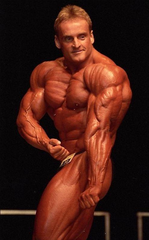 Andreas Munzer flexing his arms, chest, and shoulders on the stage, showing his outstanding physique to the judges