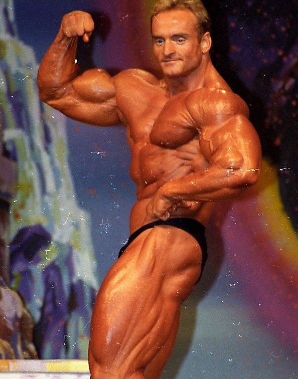 Andreas Munzer flexing his biceps on the stage